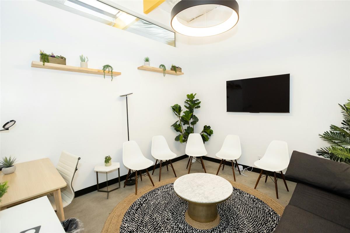 An empty, quiet clinic waiting room with white chairs and indoor plants