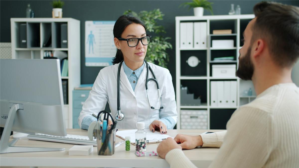 A woman doctor with a stethoscope speaking to a patient across her desk