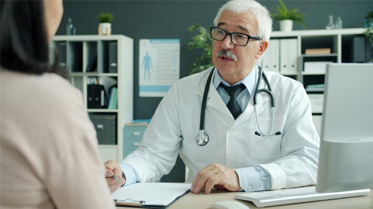 A senior doctor in a white coat explaining something to a patient in his office